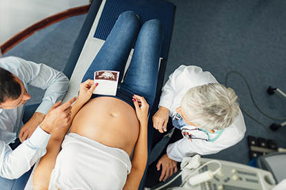 Zwangere vrouw met partner kijkt naar echo met specialist